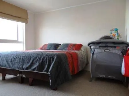 Bedroom with a queen bed, gray and red bedding, and a gray pack-n-play crib. A window is on the left.