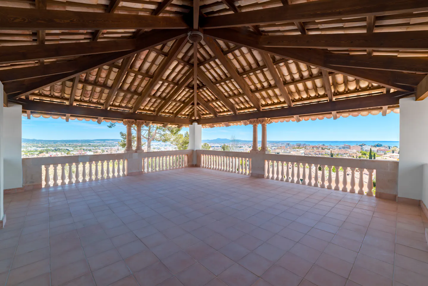 Covered patio with tile floor, stone balustrade, and wood beam ceiling. City view in the background.