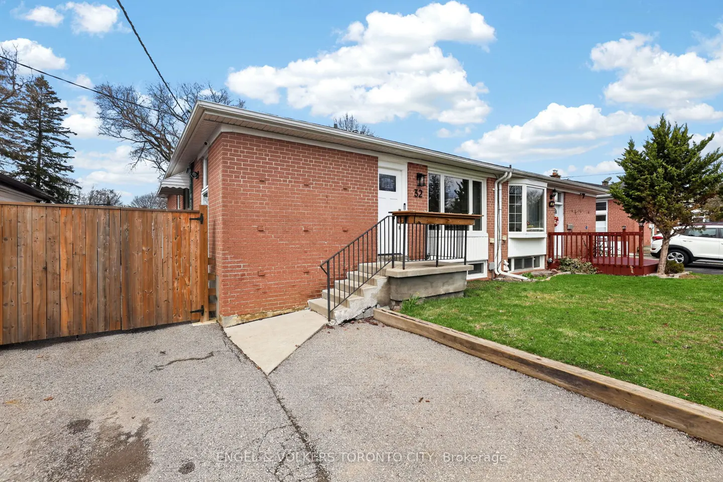 Exterior view of a red brick bungalow with a white door, black railings, and a wooden fence under a blue sky.