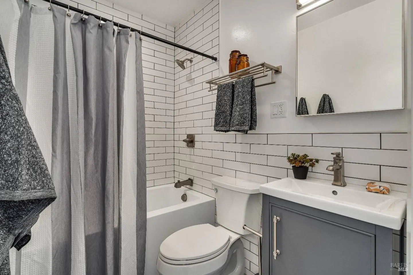 Modern bathroom with white subway tile, gray vanity, tub-shower combo, gray shower curtain, and a wall-mounted mirror.