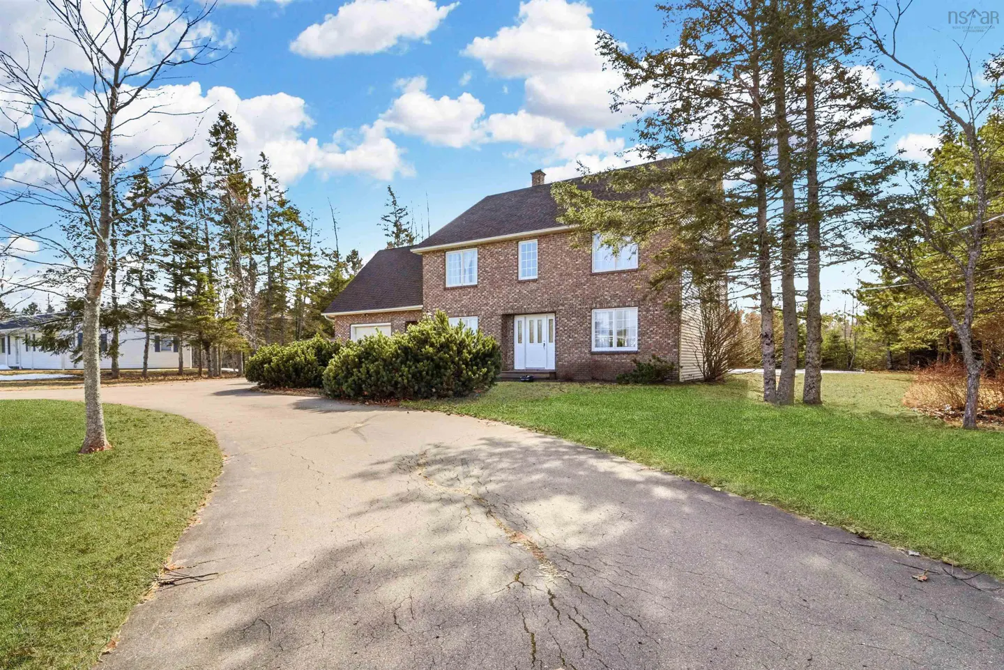 Two-story brick house with a dark roof, white trim, and a curved driveway on a sunny day.
