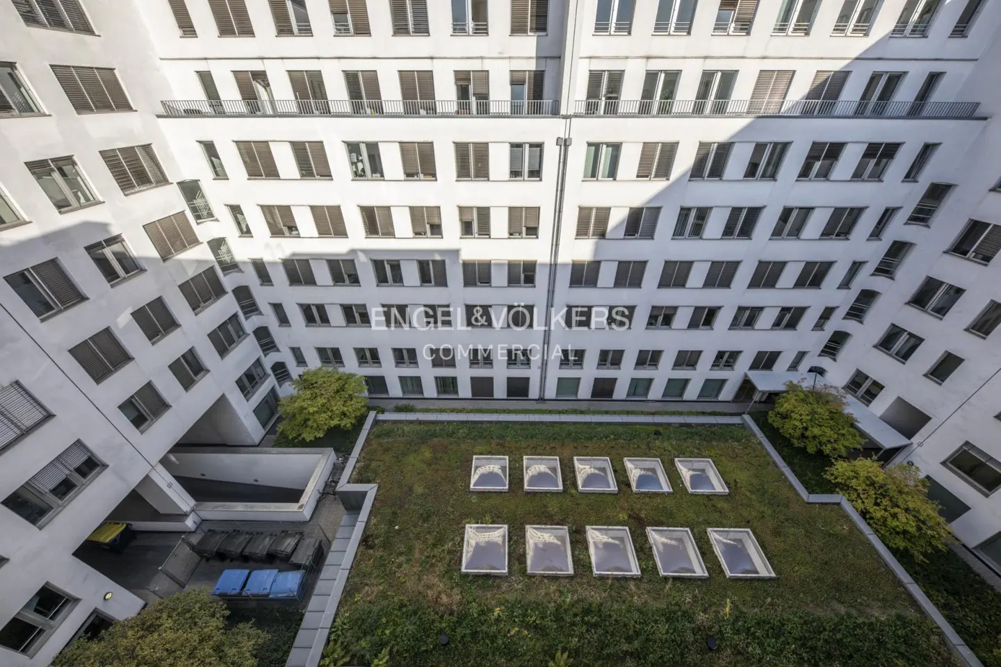 Aerial view of a white commercial building with many windows, a green roof, and the Engel & Volkers Commercial logo.
