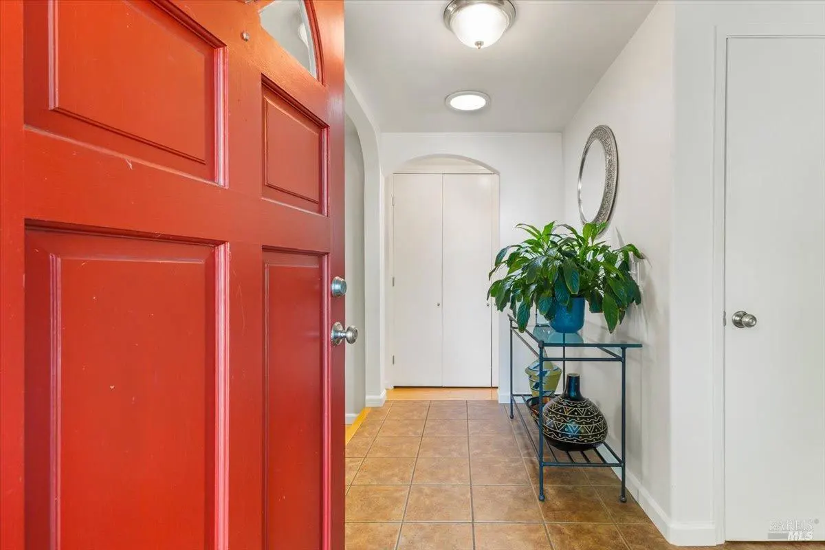Open red front door reveals a tiled foyer with a glass console table, plant, and white walls.