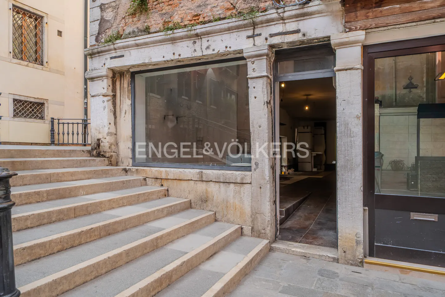 Exterior view of an Engel & Völkers real estate office in Venice, Italy. Stone steps lead to the entrance with a large window and door.