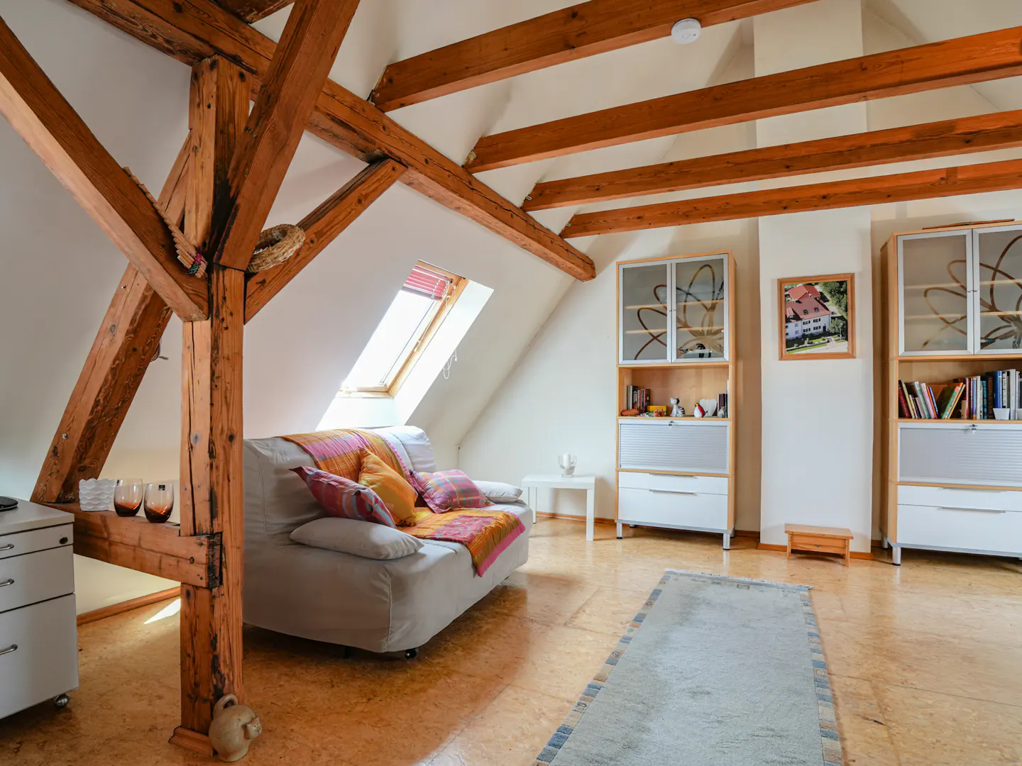 Attic living room with exposed wooden beams, a beige sofa, two tall storage cabinets, and a skylight.