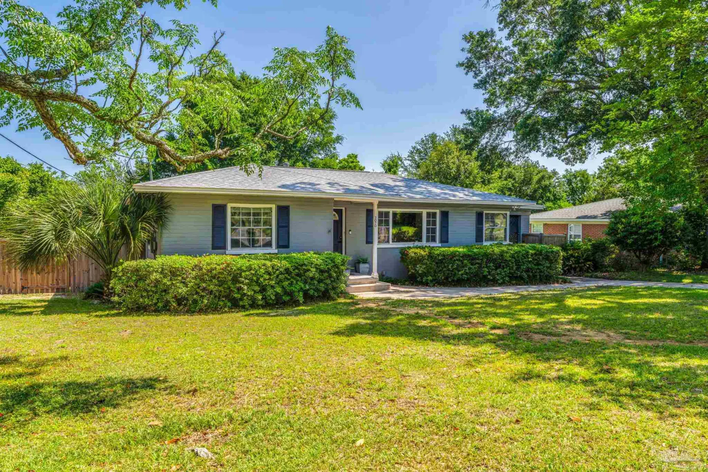 Single-story gray house with blue shutters, green lawn, and trimmed hedges on a sunny day.