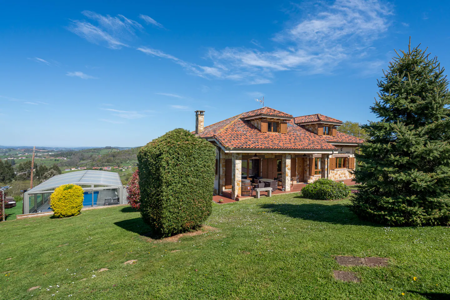 Exterior view of a house with a red tile roof, green lawn, and a covered pool in the background on a sunny day.