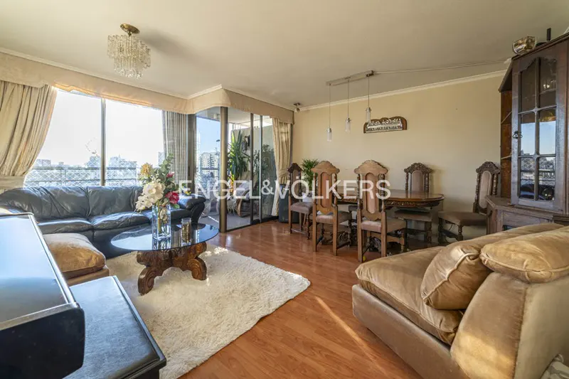 Spacious living room with wood floors, a black leather sofa, a dining table with chairs, and a large window with city views.
