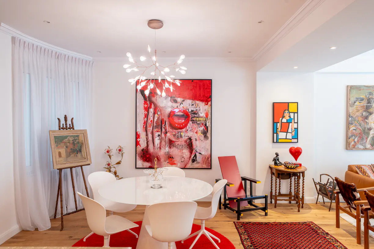Bright dining room with white walls, wood floors, and modern art. A white table sits on a red rug, lit by a branch chandelier.