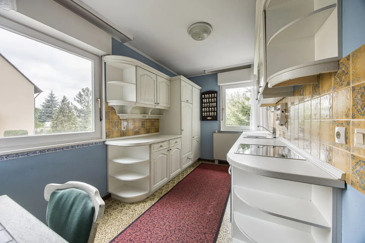 A kitchen with white cabinets, blue walls, and a red rug.