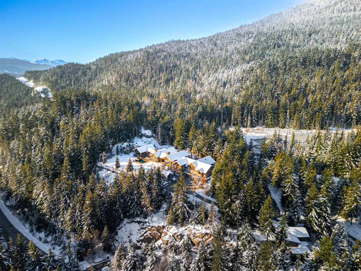 Aerial view of a large, multi-unit log cabin home nestled in a snowy evergreen forest on a sunny day.