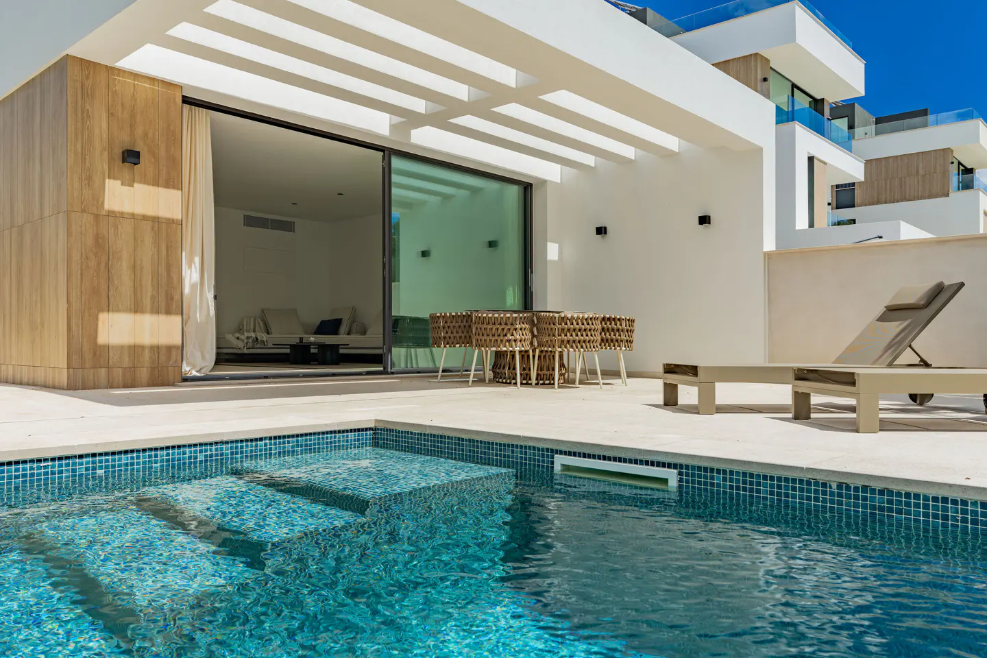 Outdoor patio with a pool, table, and lounge chair. Sliding glass doors lead to a bright, modern interior.