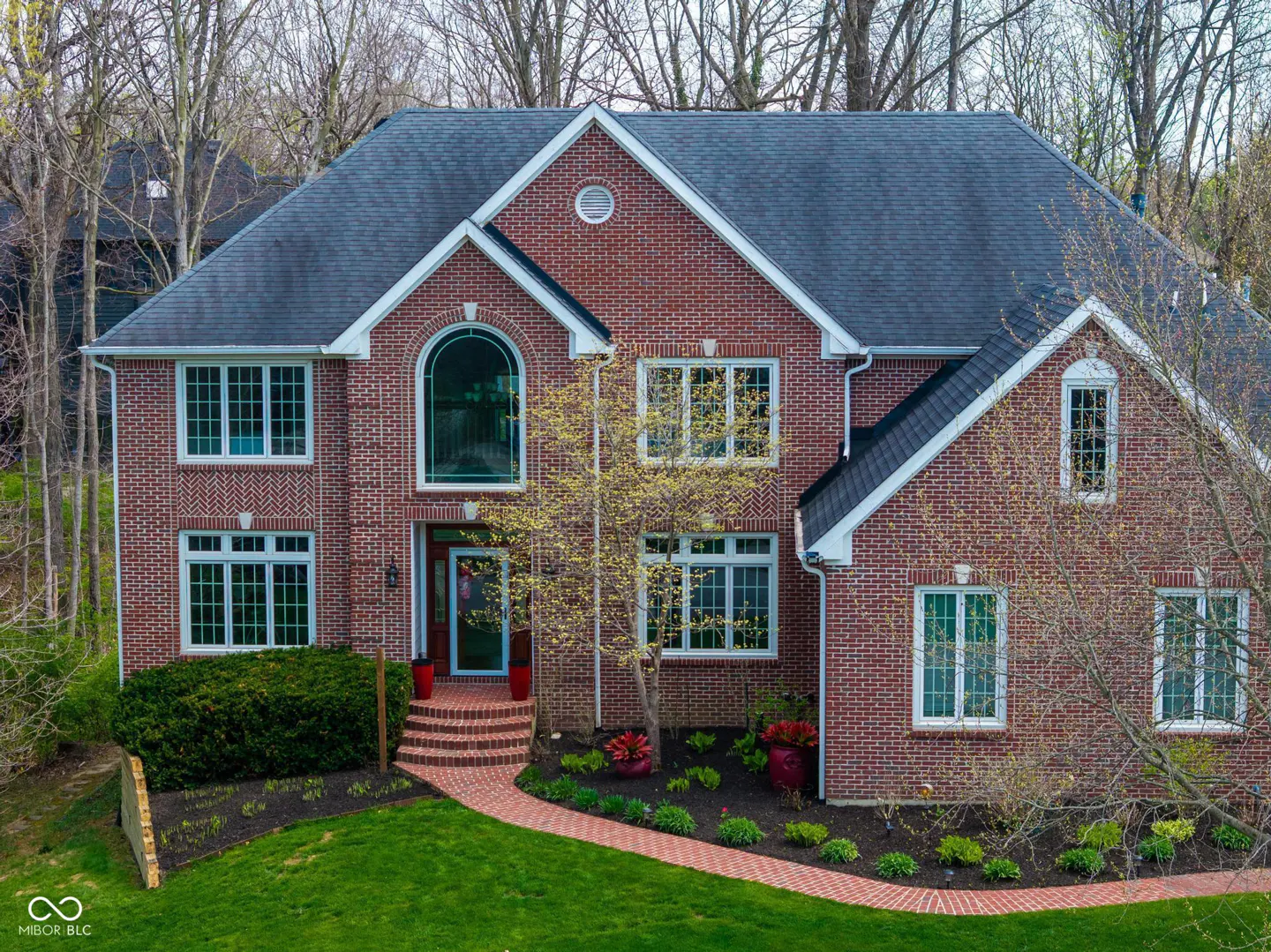 Two-story brick house with a gray roof, white trim, and a brick walkway leading to the red front door.