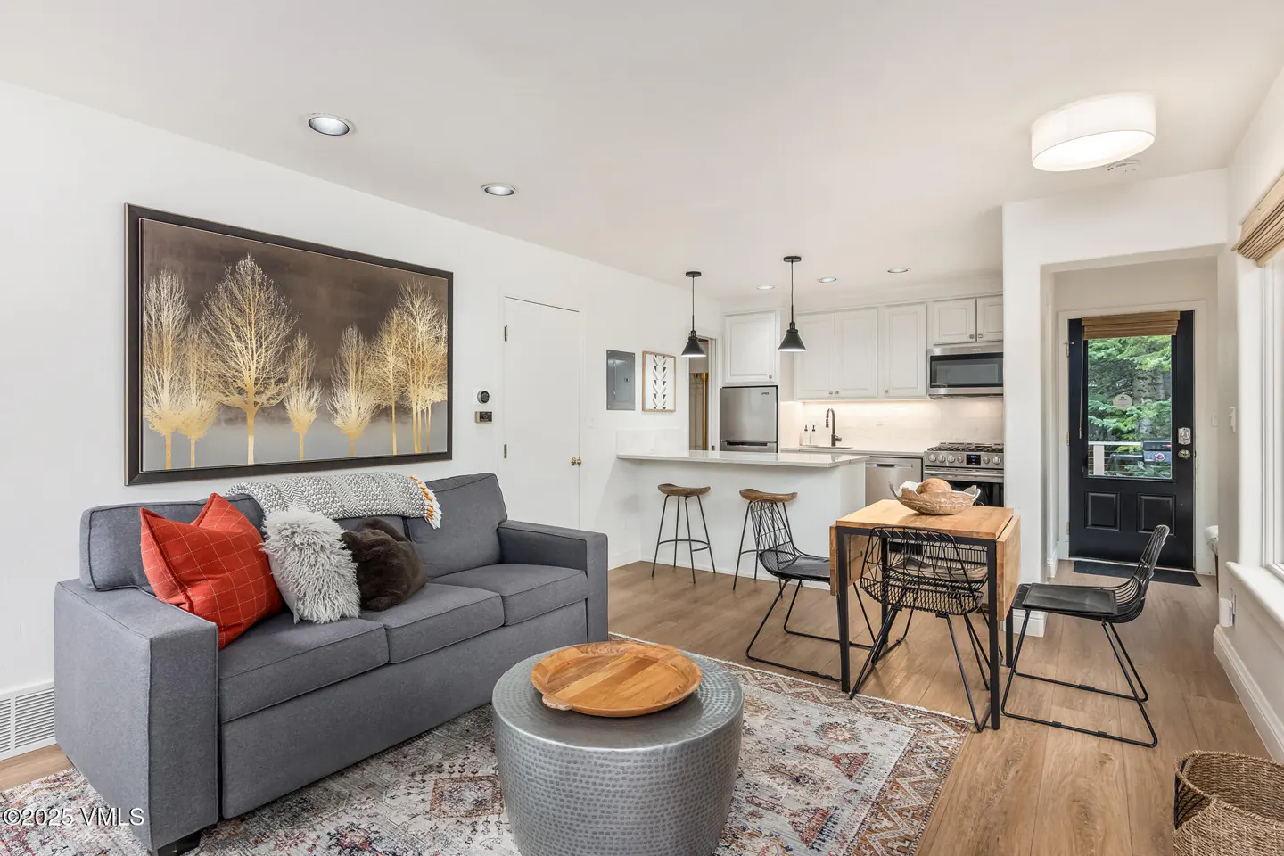 A modern living space with a gray sofa, a painting of gold trees, and a white kitchen in the background.