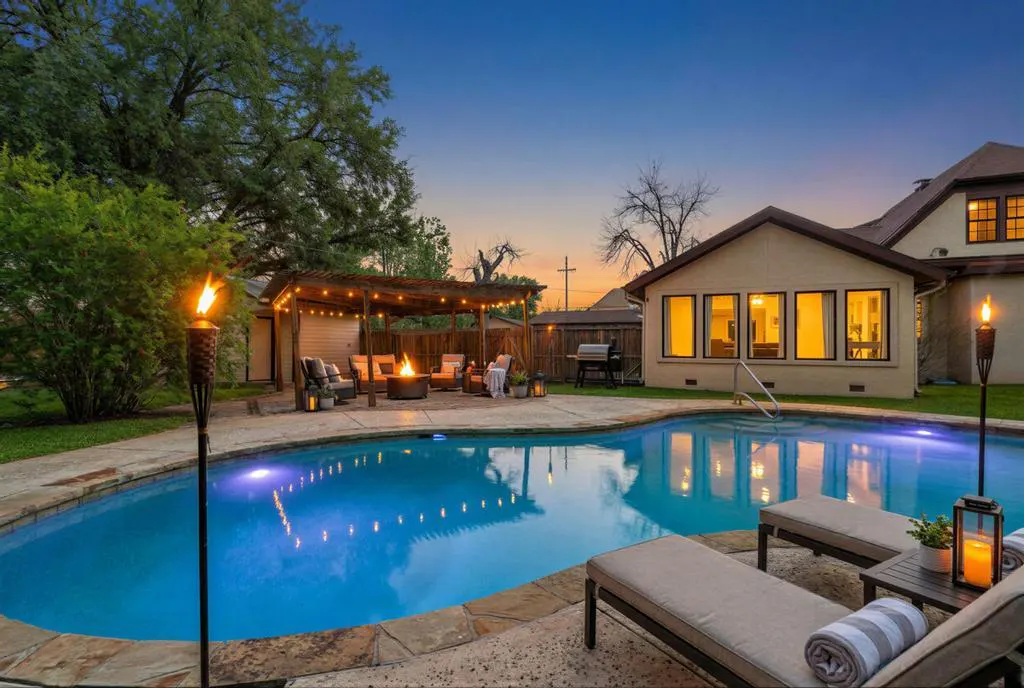 Backyard pool at dusk with tiki torches, lounge chairs, and a pergola with a fire pit.
