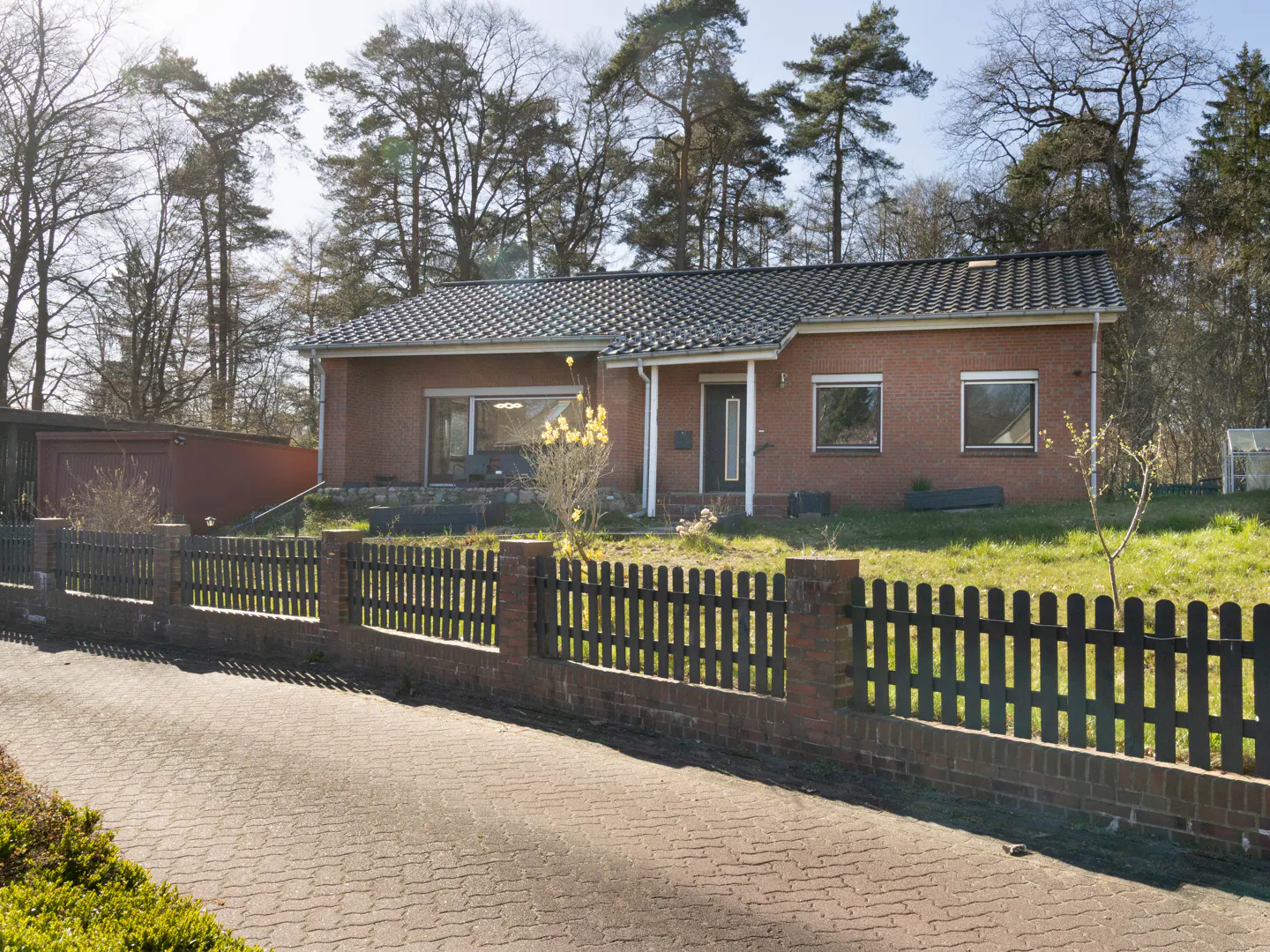 A single-story red brick house with a black roof and a black picket fence.