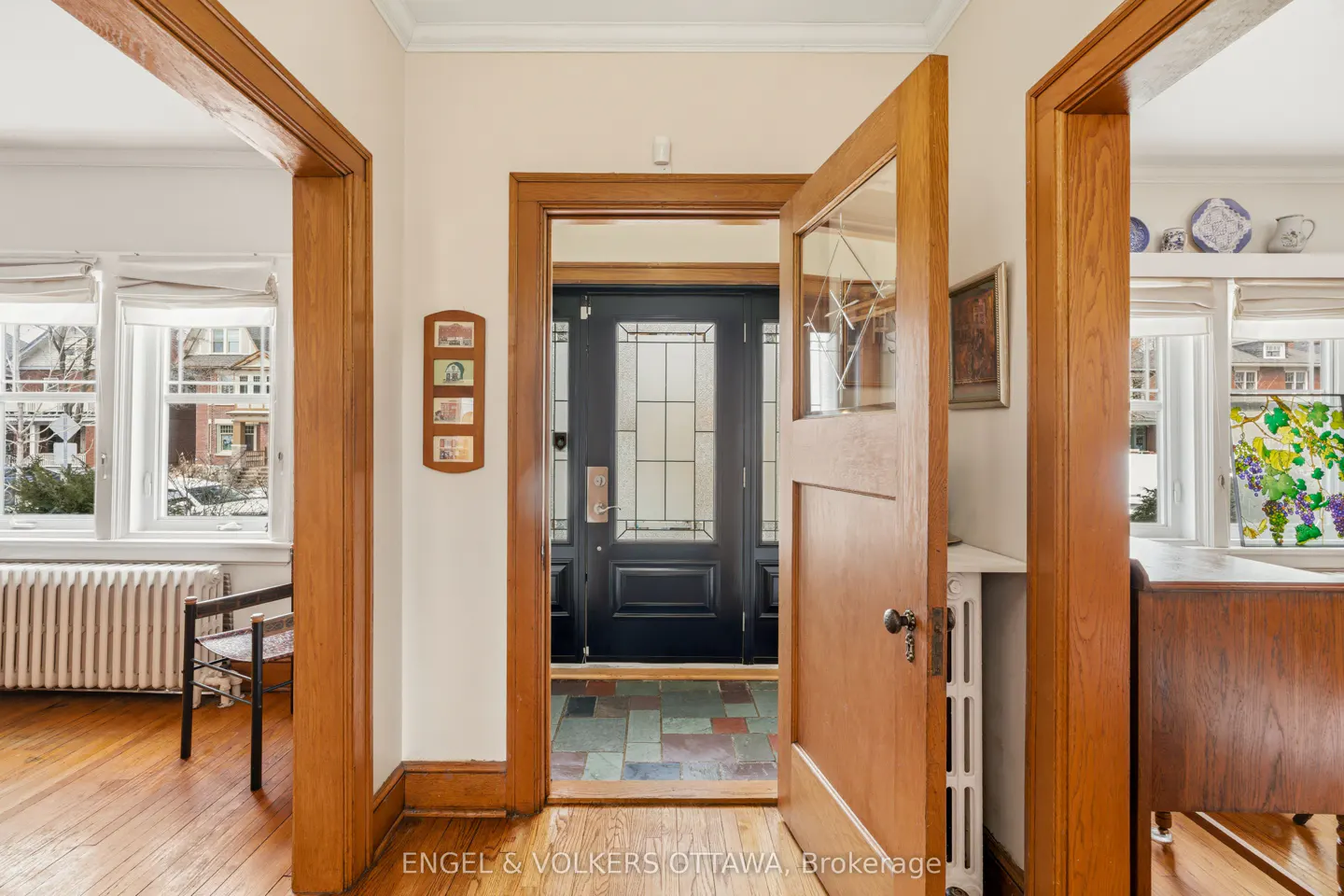 A foyer with hardwood floors and wood trim. An open wood door leads to a black front door with glass panels. Windows are visible in adjacent rooms.