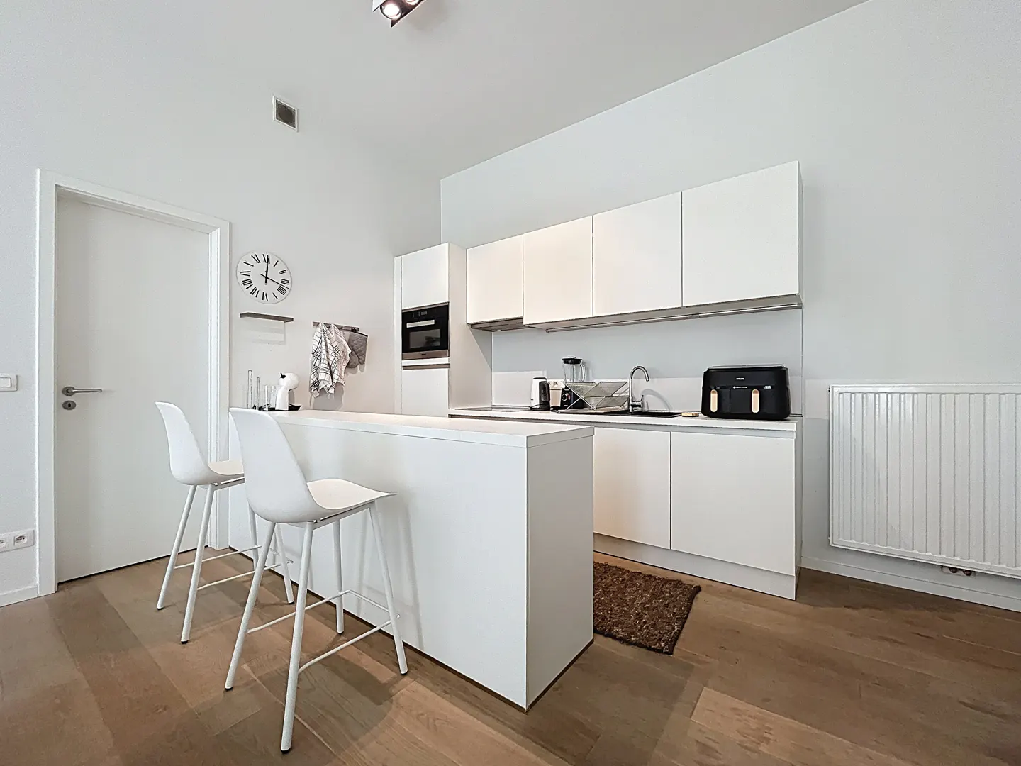 Bright, modern kitchen with white cabinets, island, and two white bar stools on a wood floor.