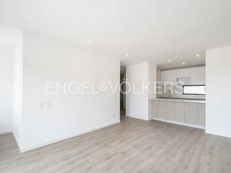 Modern open-plan living area with white walls, light wood flooring, and a kitchen with white cabinets and a wood island.
