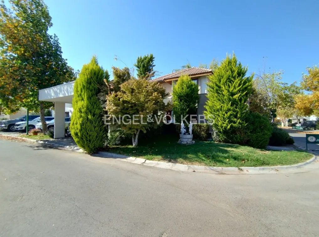Exterior view of a two-story house with a carport, surrounded by green trees and grass under a clear blue sky.
