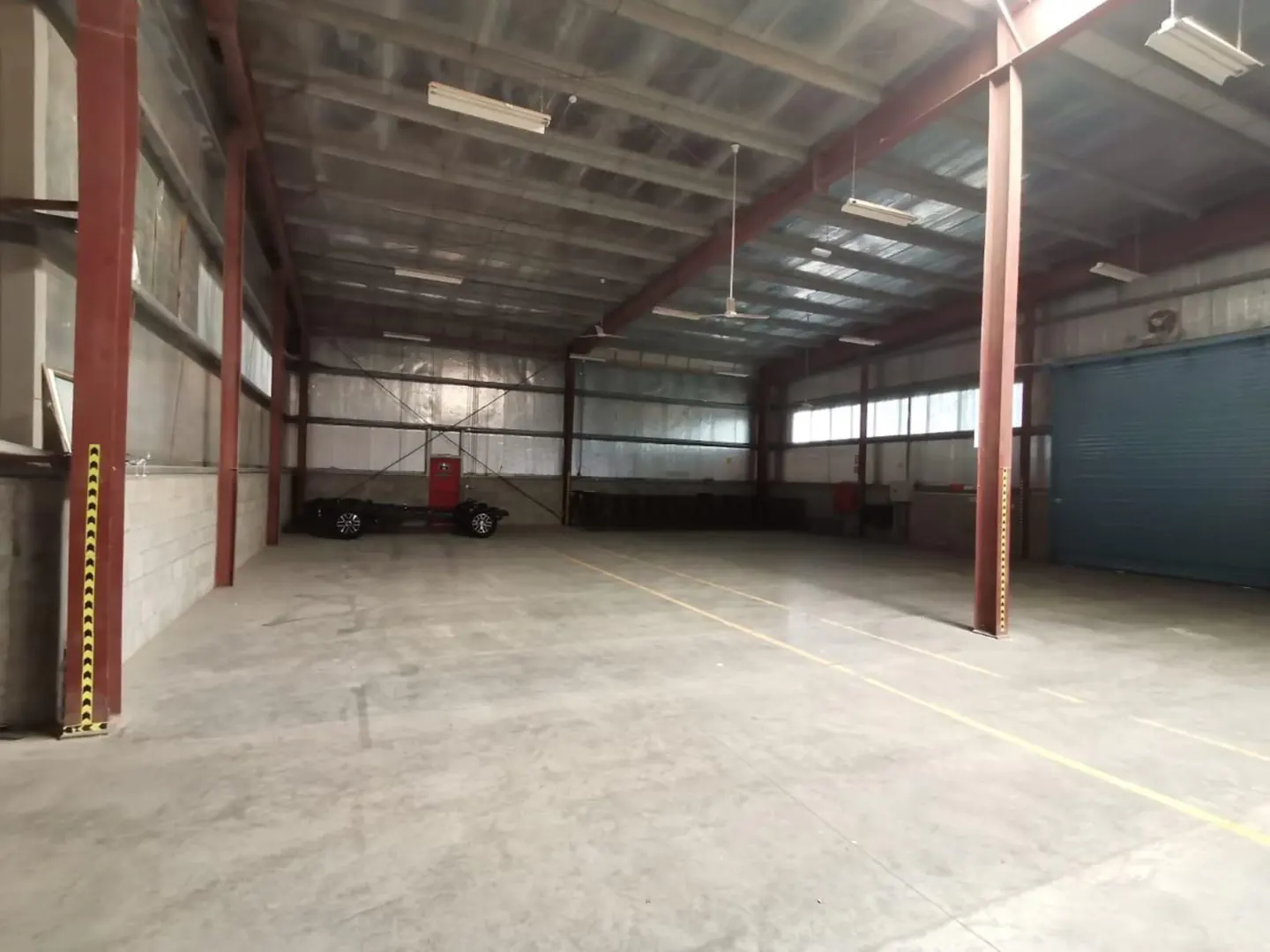 A large, empty warehouse with a concrete floor, metal beams, and a truck chassis in the background.