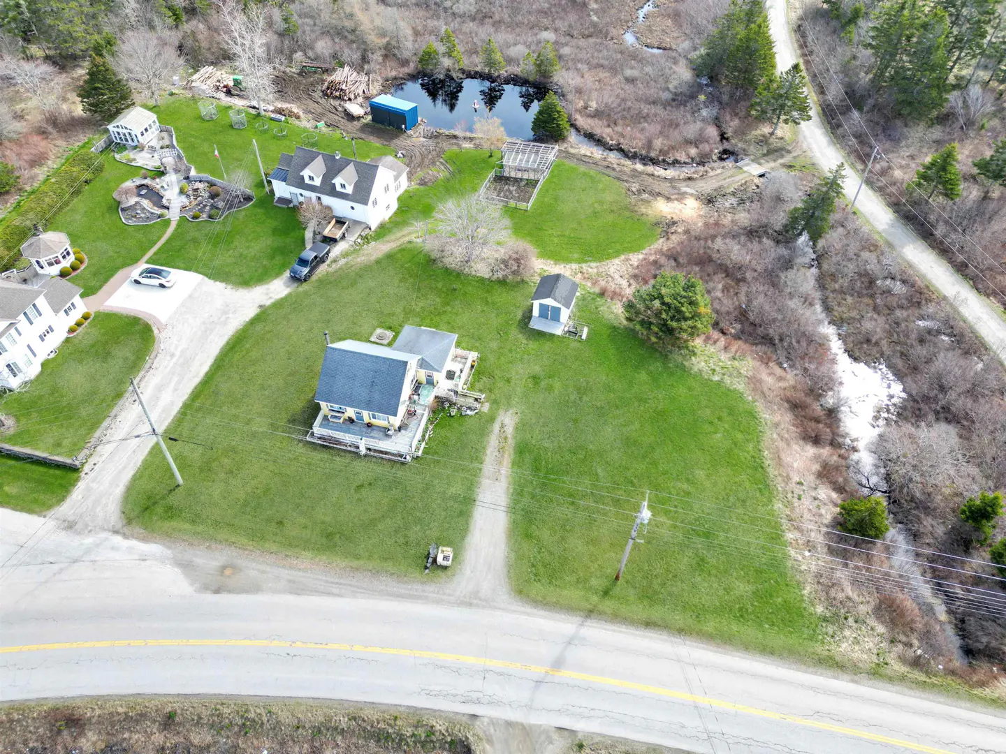 Aerial view of a property with a yellow house, green lawn, pond, and other buildings.