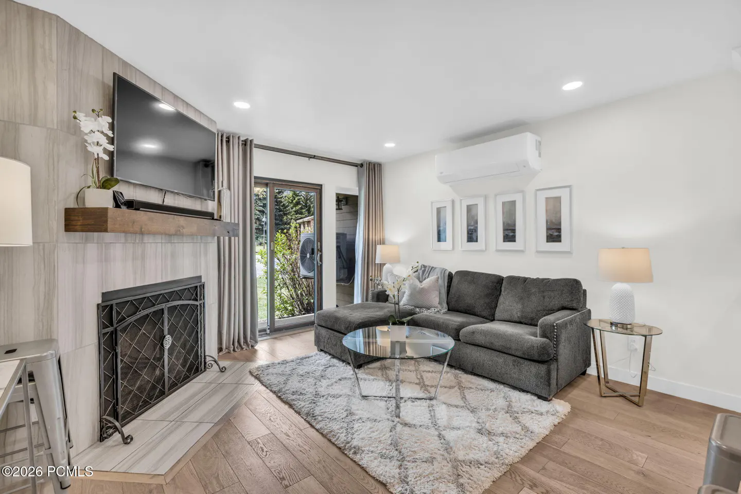 Living room with gray sectional sofa, glass coffee table, fireplace with TV, and sliding glass doors to a patio.