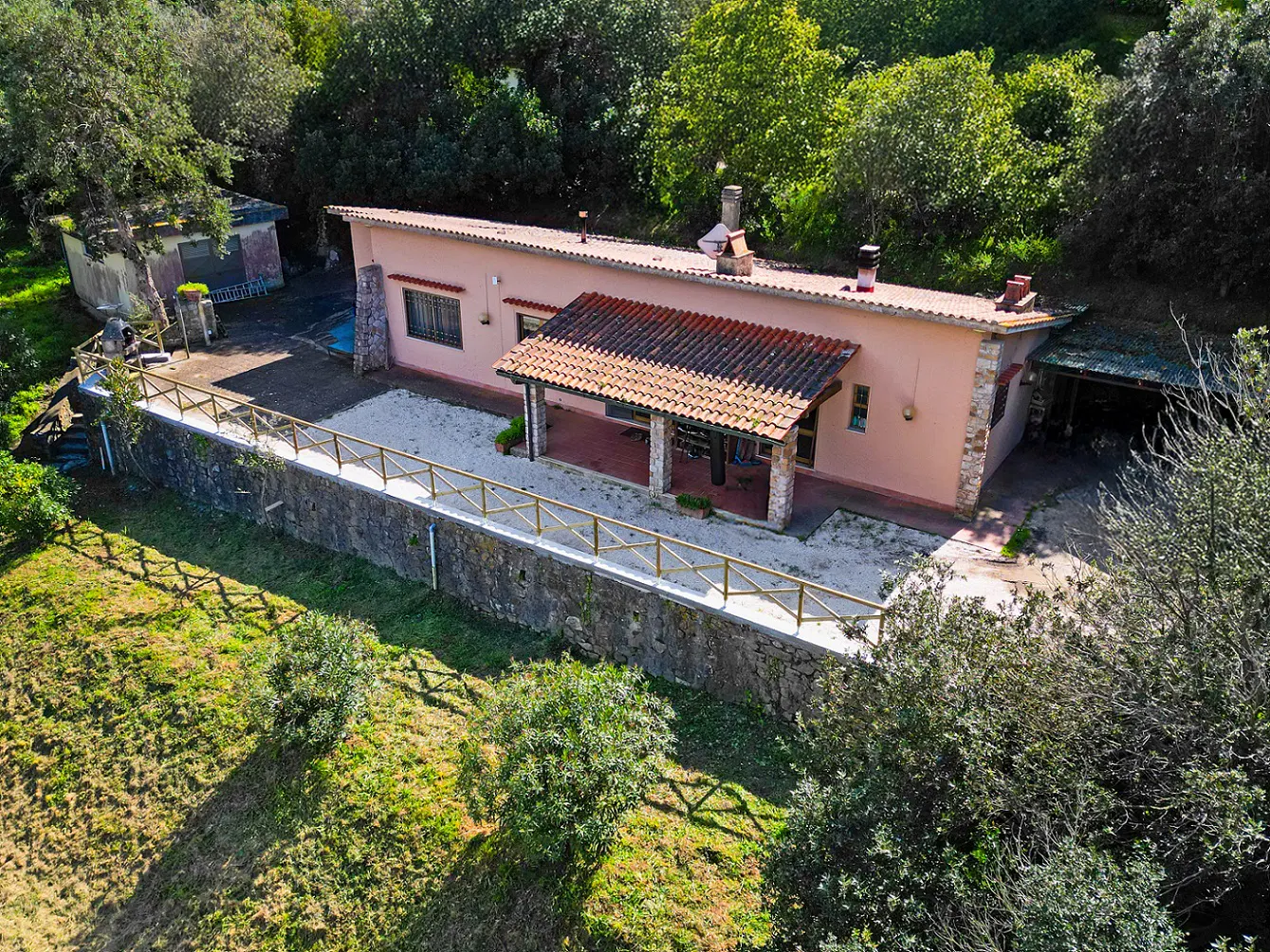 Aerial view of a one-story peach house with a red tile roof, stone accents, and a covered porch, surrounded by lush greenery.