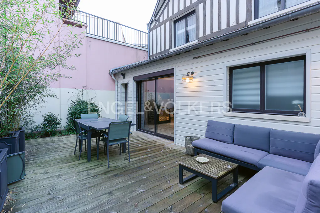 Outdoor patio with a gray table and chairs, a blue sofa, and a wooden deck. The house has white siding and black trim.