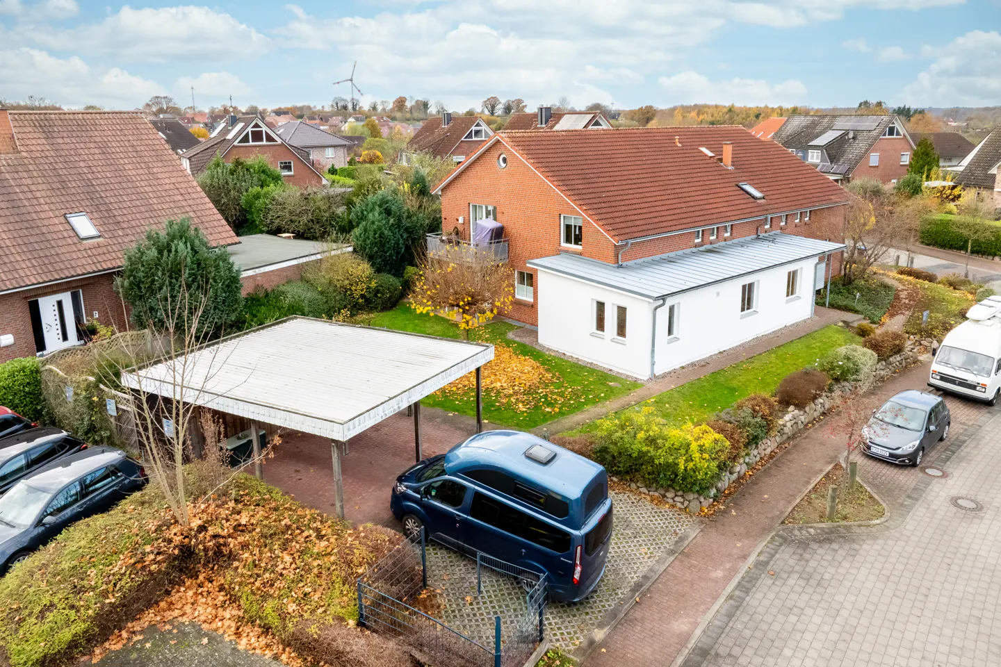 Aerial view of a residential area with brick houses, cars, and a blue camper van parked under a carport.