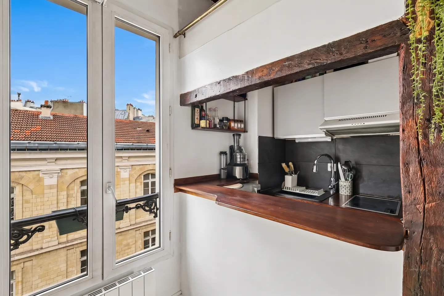 A small kitchen with a wooden countertop, white cabinets, and a window overlooking a cityscape.
