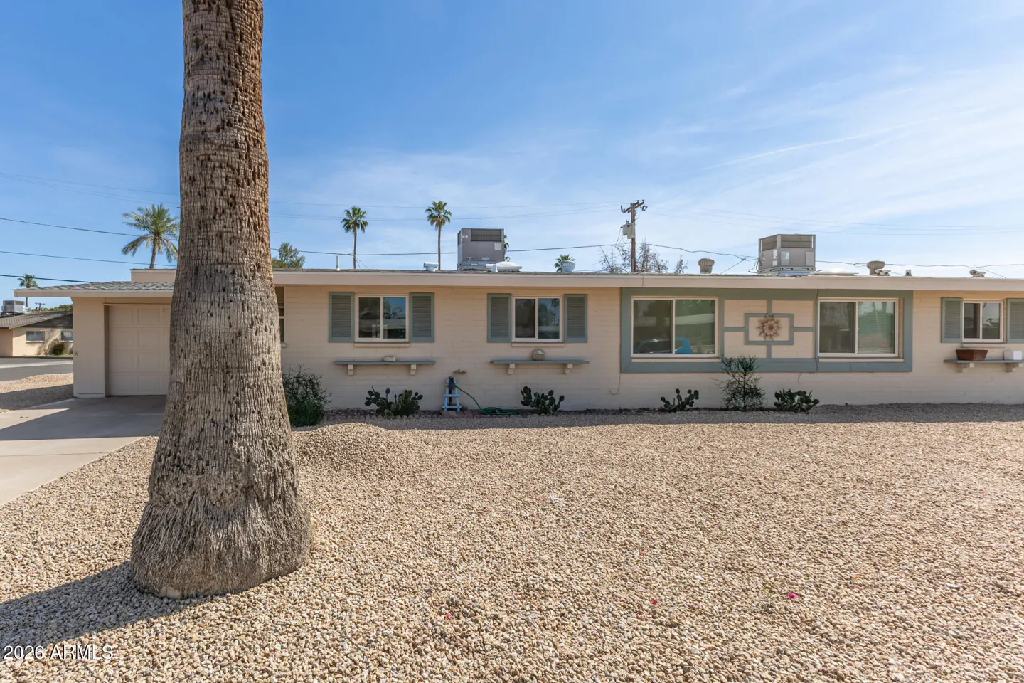 Tan single-story home with light blue trim and a gravel yard. A palm tree is in the foreground.