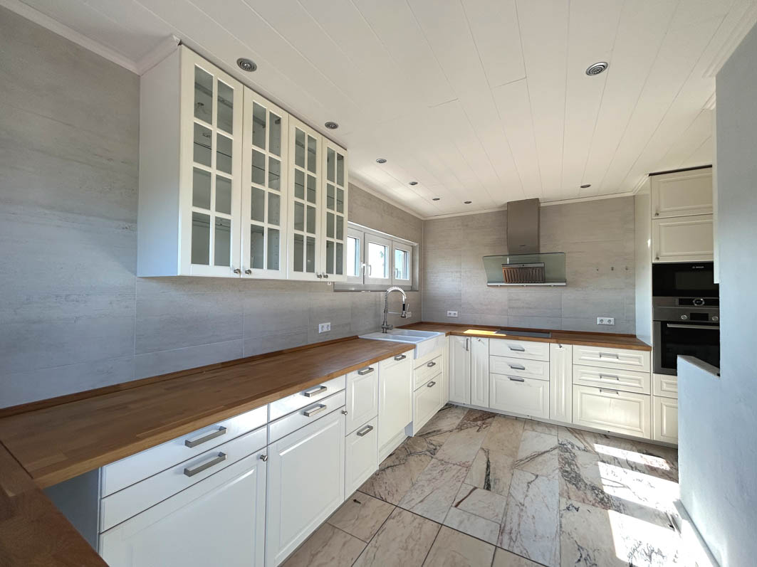 Bright kitchen with white cabinets, wood countertops, and marble tile floor. Stainless steel range hood and built-in oven.