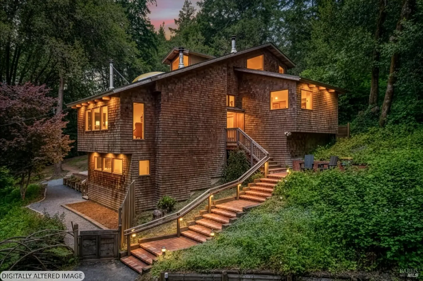Exterior view of a three-story wood shingle house with brick steps and a metal railing leading to the front door. The house is surrounded by trees.