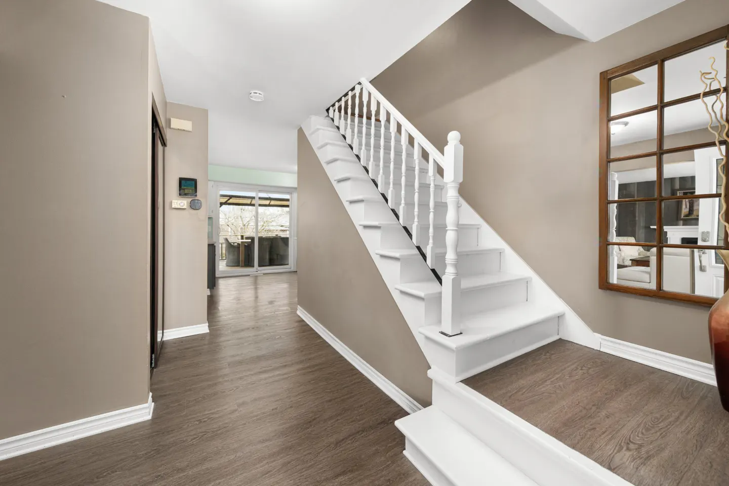 Foyer with wood-look floors, beige walls, and white trim. A white staircase leads up. A large, multi-pane mirror hangs on the wall.