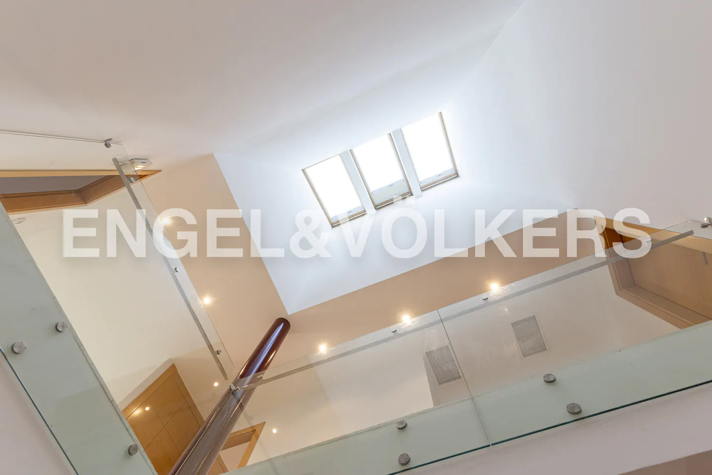 Interior view of a modern home featuring a glass railing staircase and a skylight.