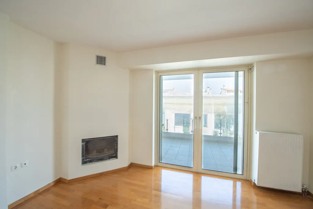 Bright, empty room with hardwood floors, white walls, fireplace, and sliding glass doors to a balcony.