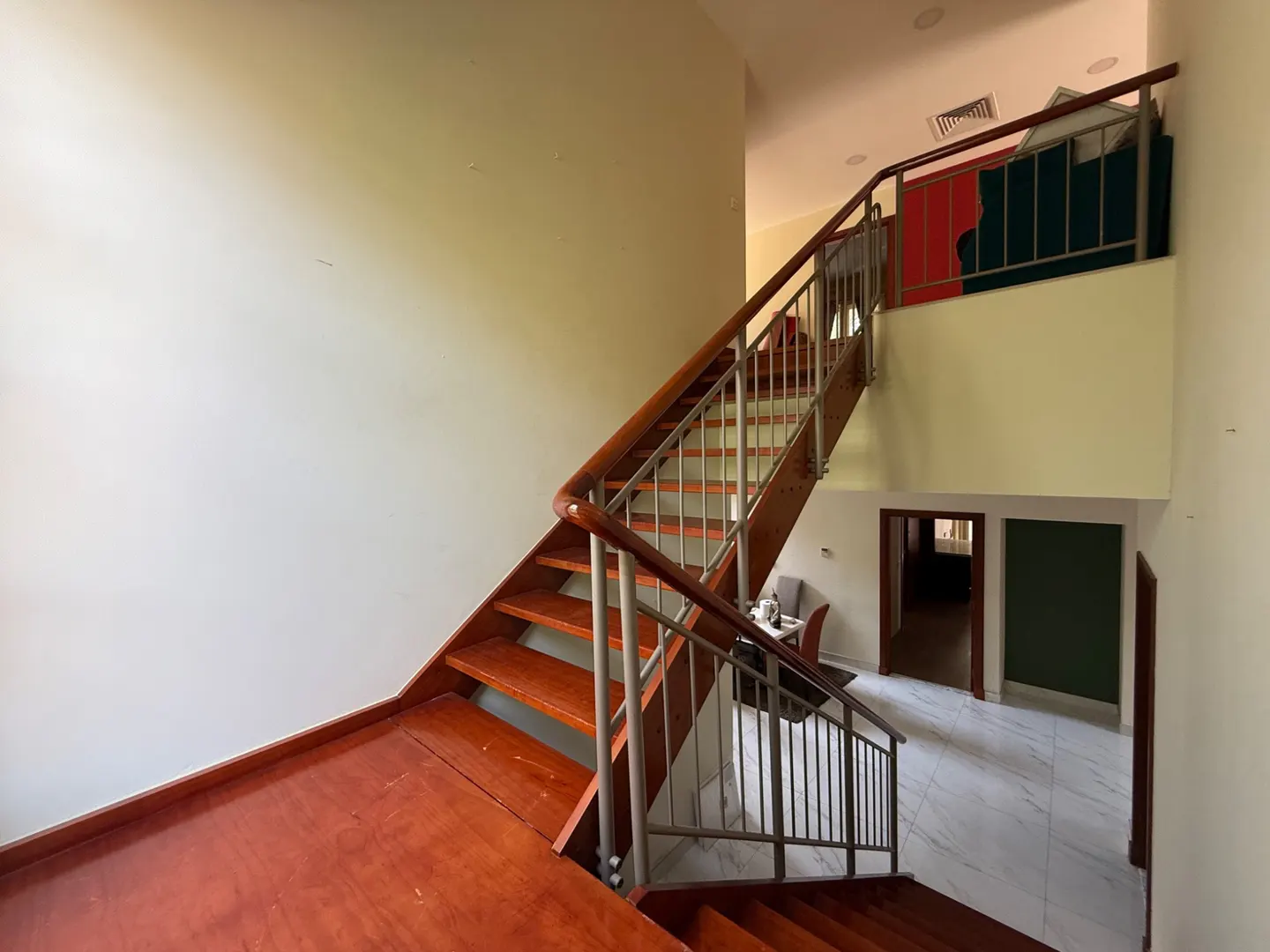 Interior view of a home featuring a wooden staircase with metal railings, leading to an upper level with a colorful art piece.