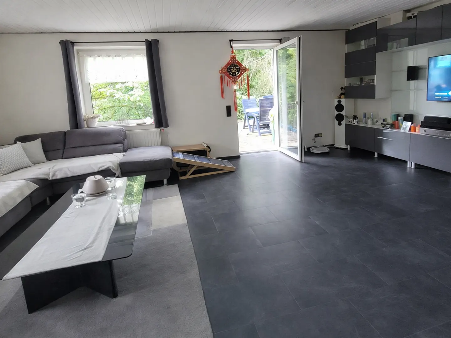 A living room with a gray sectional sofa, a glass coffee table, and an open door to a patio.
