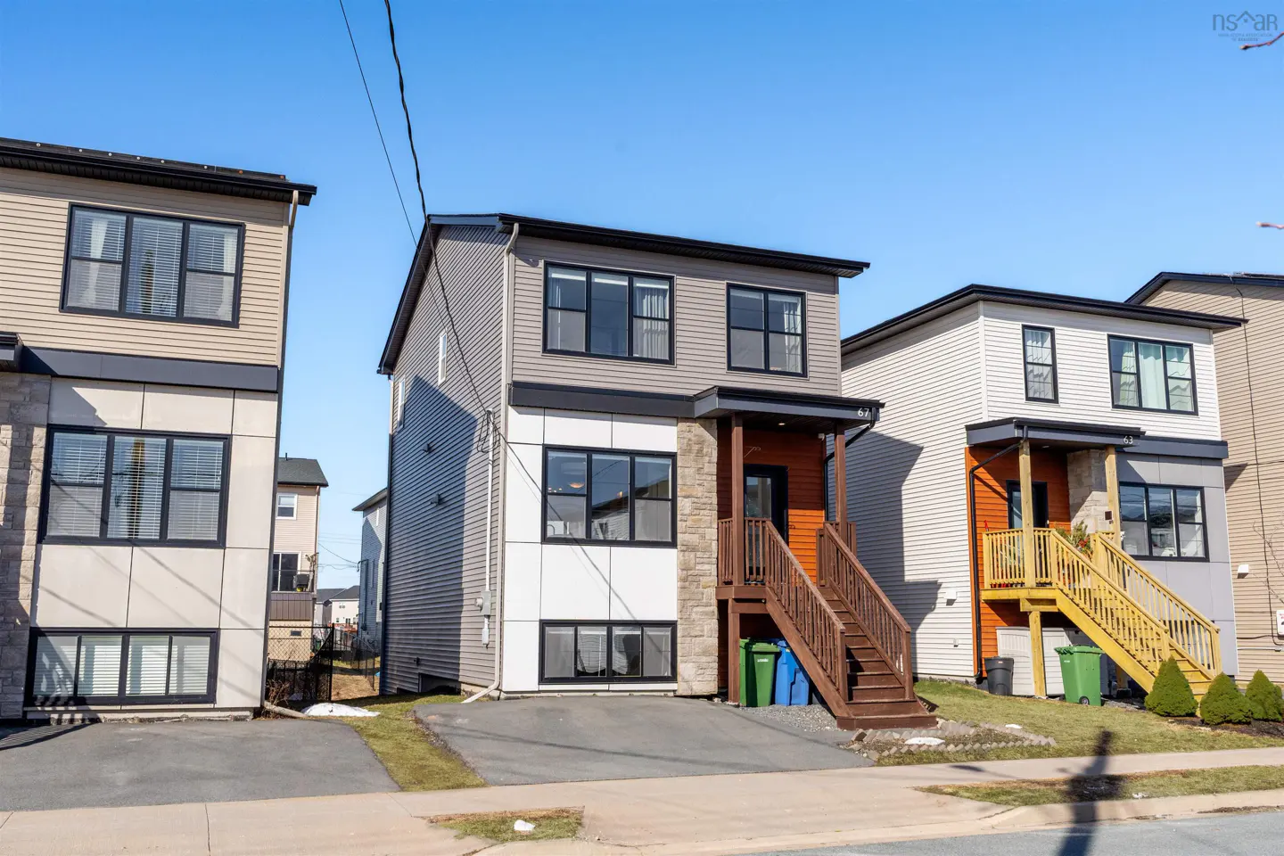 Two-story house with gray siding, white panels, and stone accents. Brown stairs lead to a wood-paneled porch. Blue sky background.