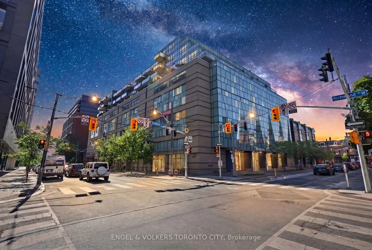Modern glass-fronted apartment building at a city intersection under a vibrant, star-filled night sky.