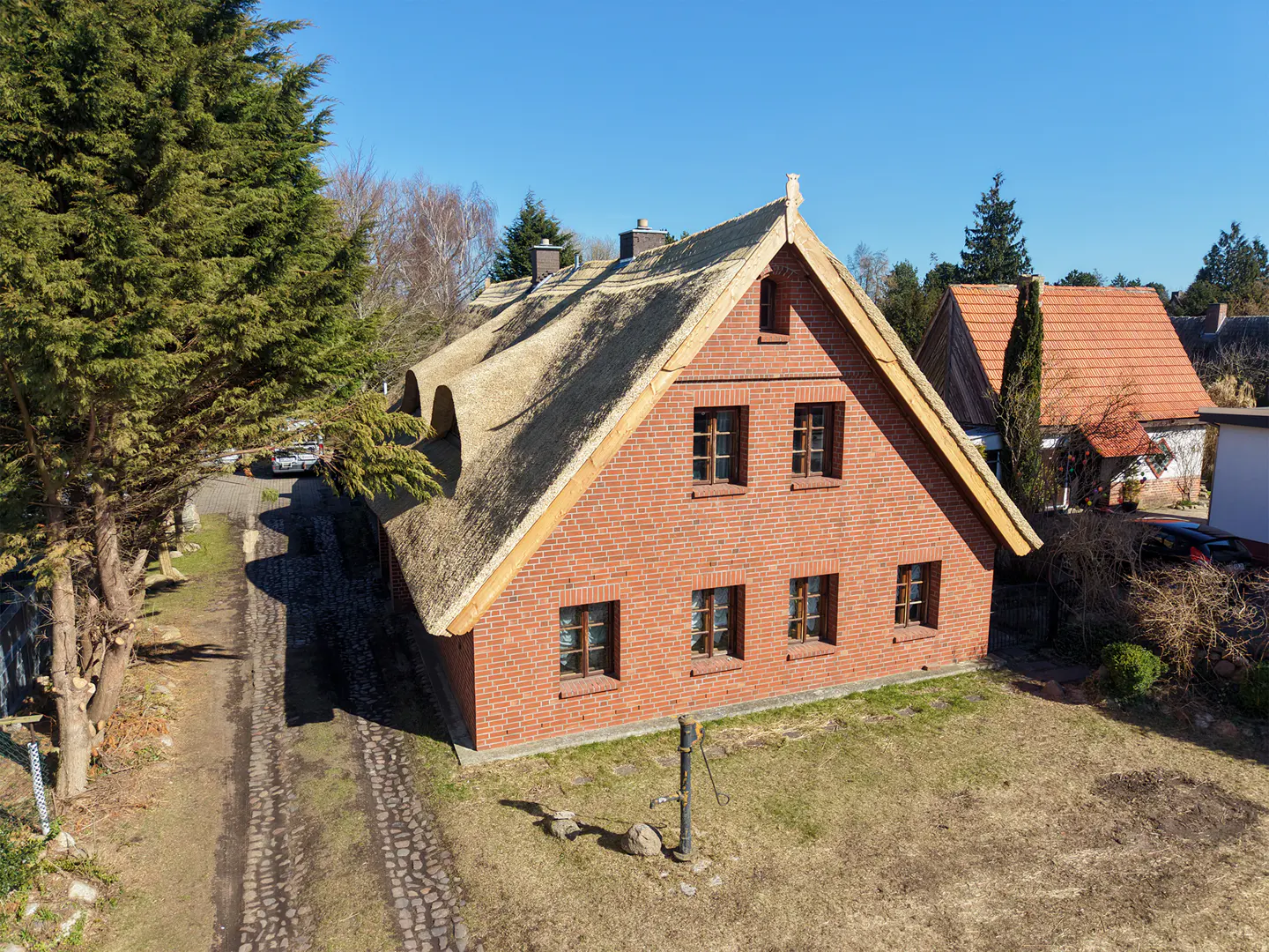 A two-story brick house with a thatched roof and brown window frames on a sunny day.