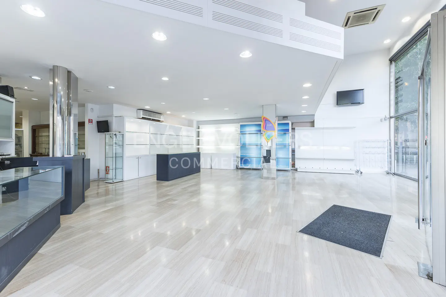 Bright, empty commercial space with marble floors, white walls, display cases, and a gray welcome mat near the glass entrance.
