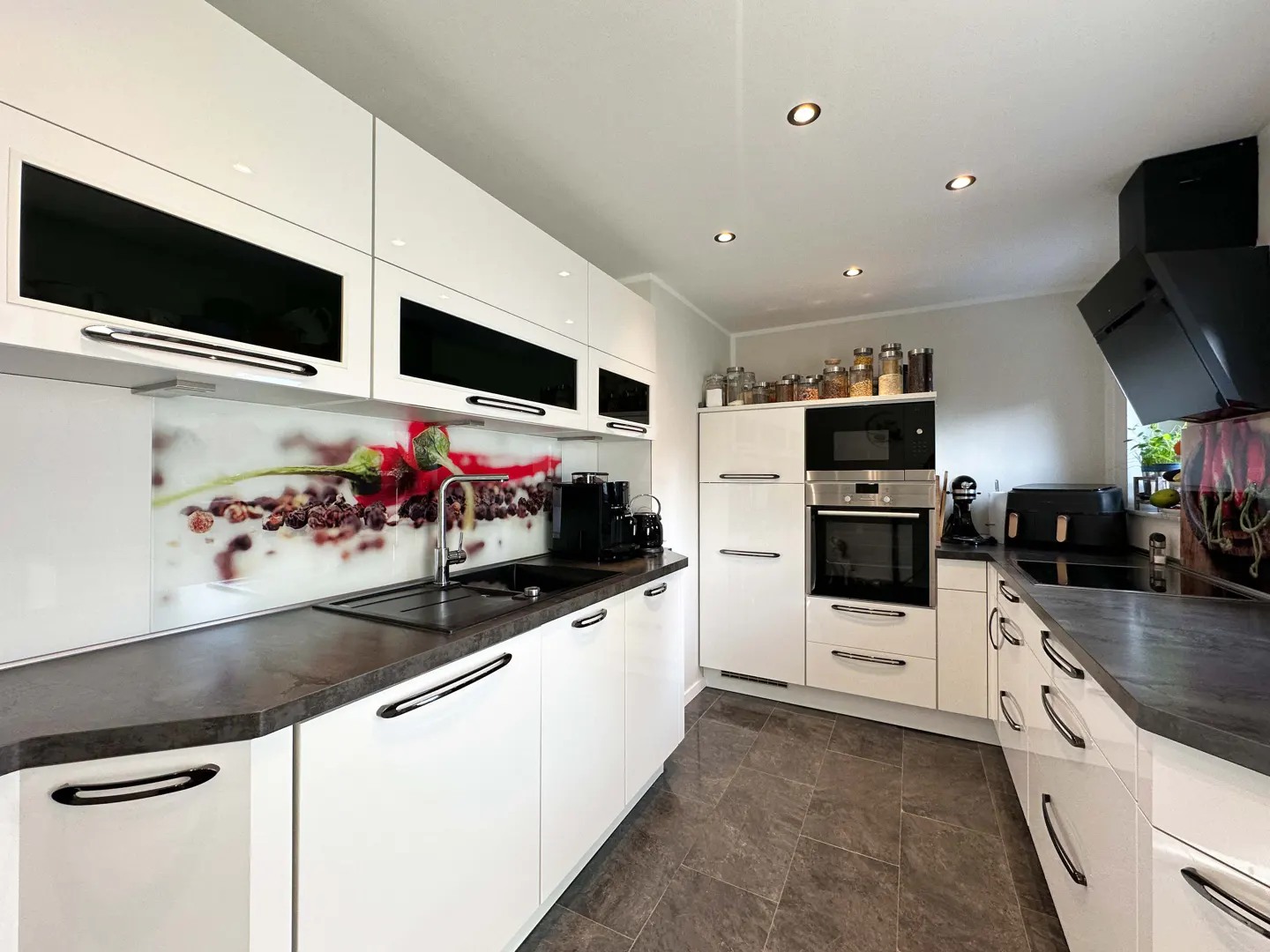 Bright kitchen with white cabinets, black countertops, and a backsplash with a coffee bean design. Appliances include a built-in oven and microwave.