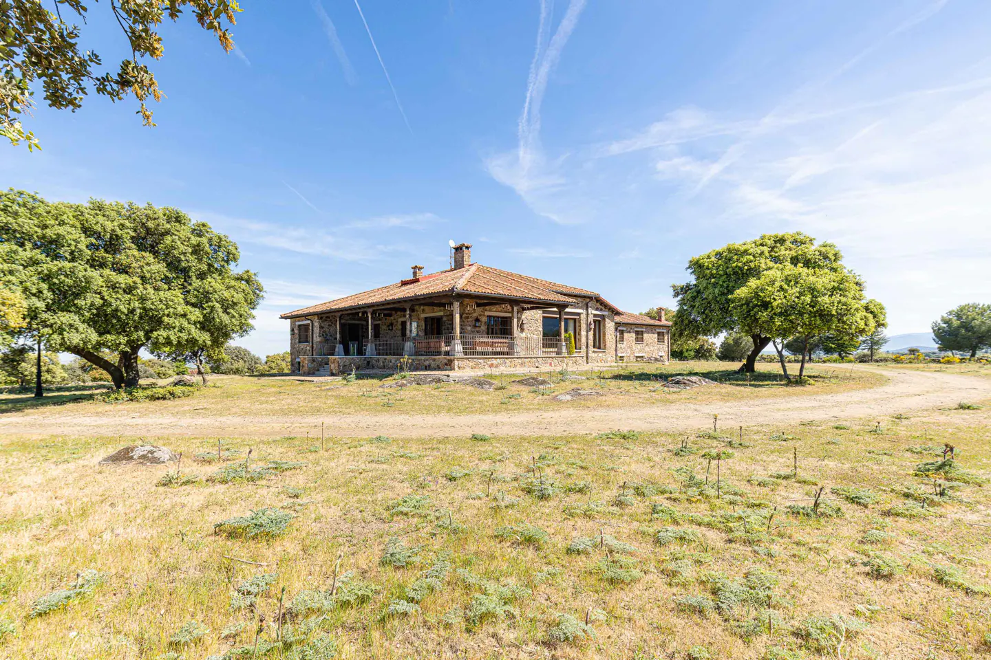 A stone house with a red tile roof sits on a grassy field under a blue sky.