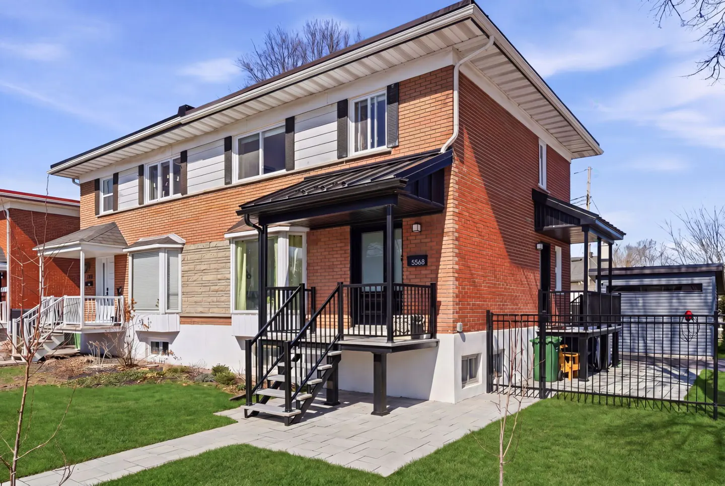 Exterior view of a two-story red brick house with black shutters and a black metal porch roof.