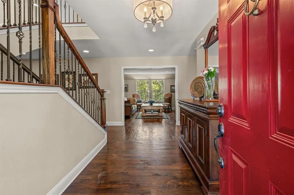 Open red front door reveals a foyer with hardwood floors, stairs, and a glimpse into the living room.