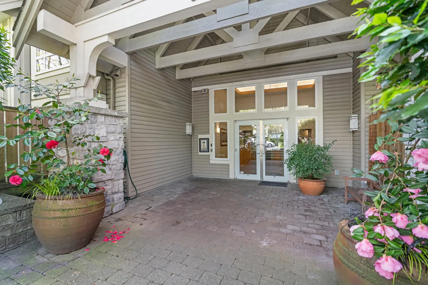 Exterior view of a building entrance with double glass doors, potted flowers, and a stone walkway.
