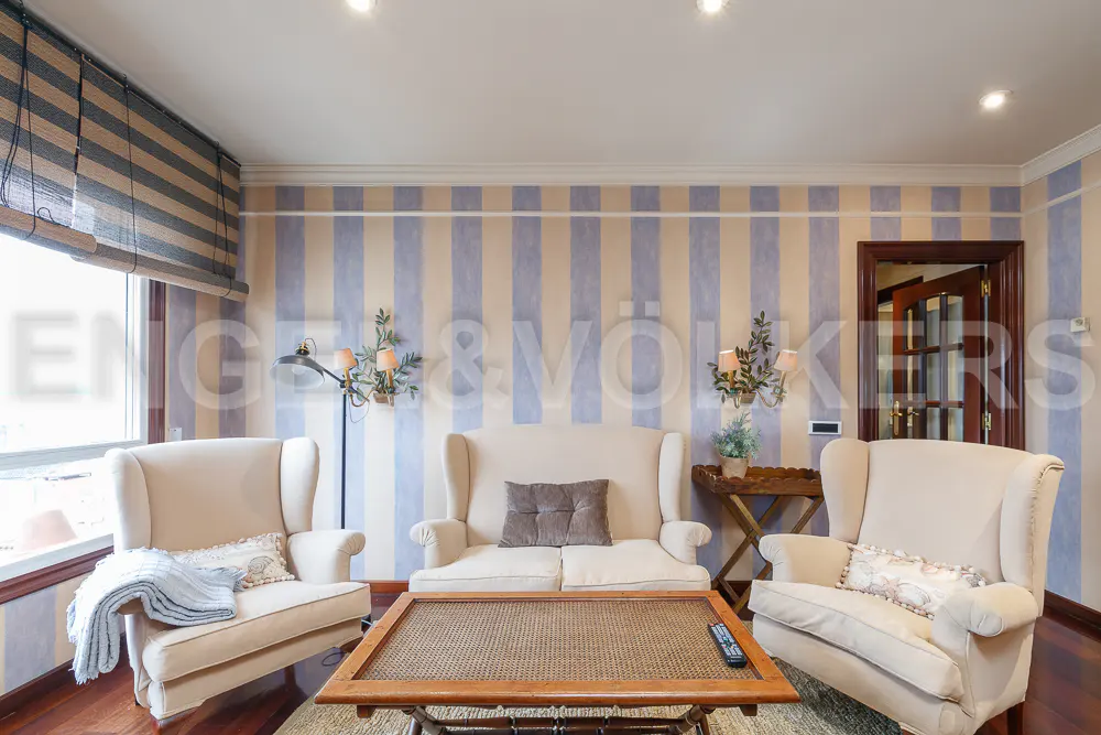 Living room with two cream wingback chairs, a matching sofa, a wooden coffee table, and blue and beige striped wallpaper.