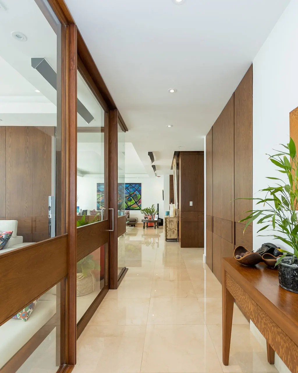 Hallway with beige tile floor, wood-framed glass doors, and a wooden console table with a potted plant.